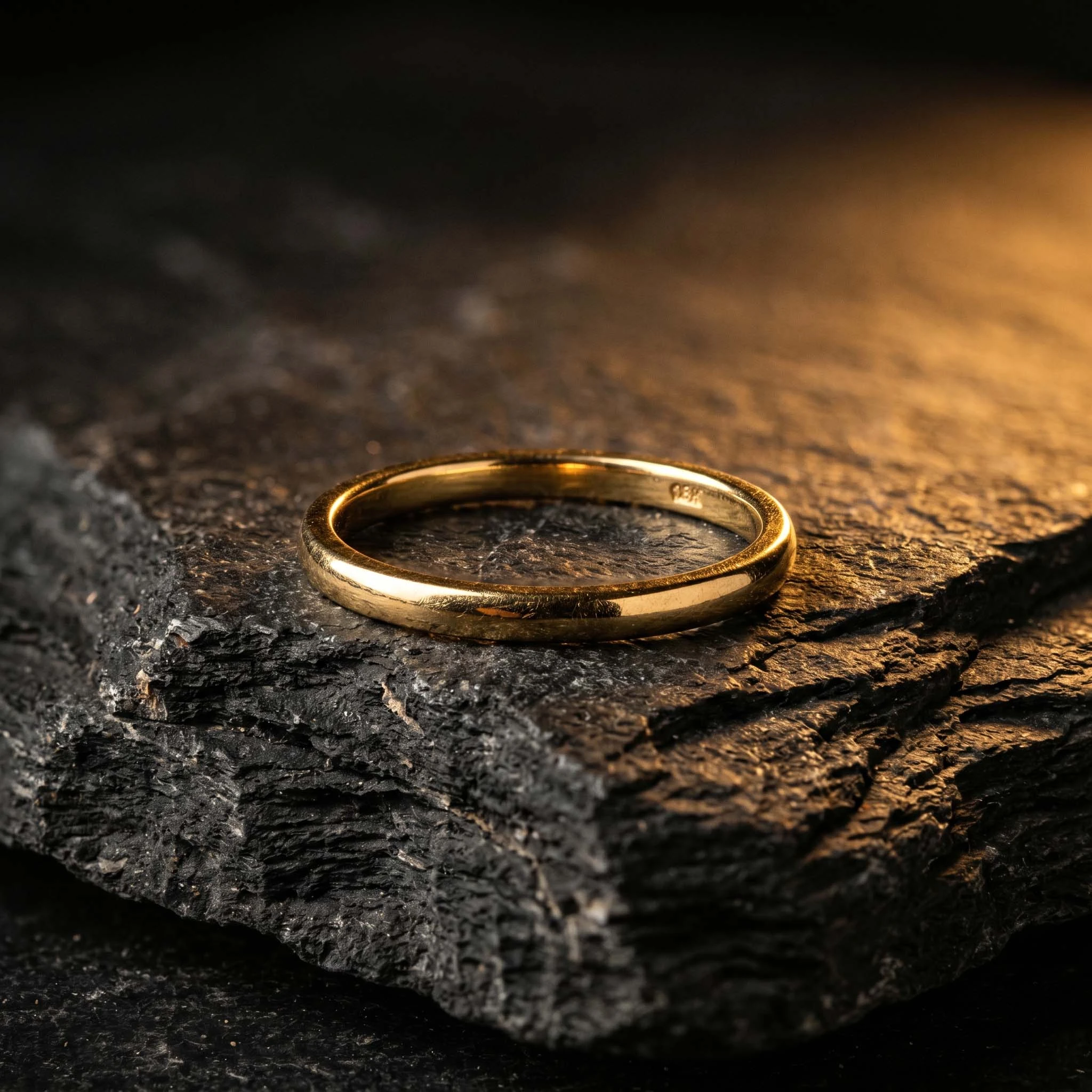 Bague anneau classique en or lisse posée sur une pierre noire texturée.